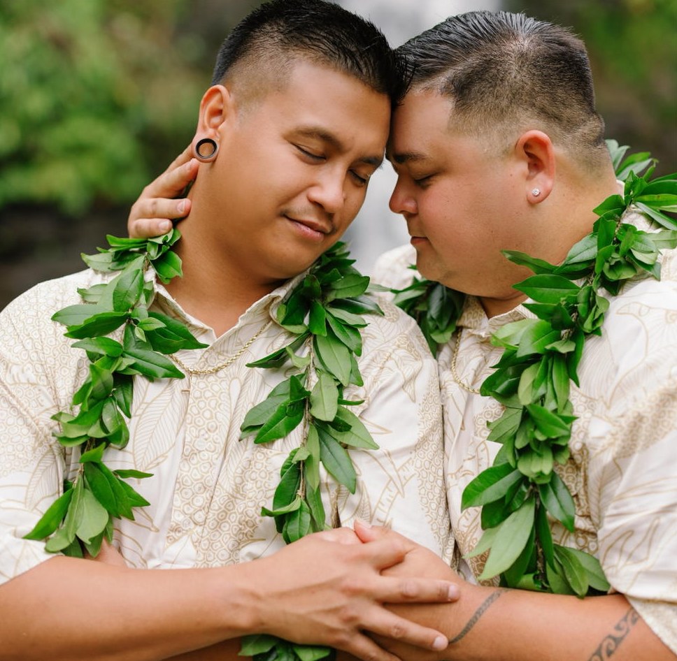 Tylor and Austin resting foreheads together, hands clasped, wearing maile lei